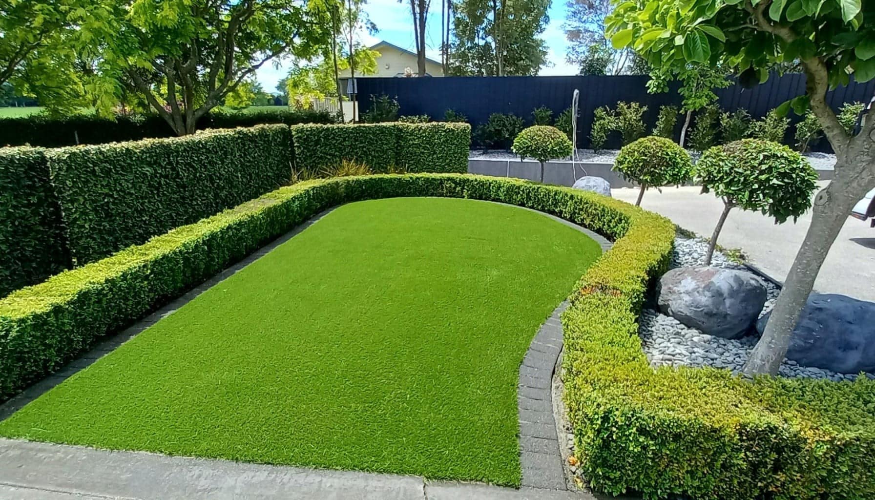 Artificial grass lawn with neatly trimmed hedge border in a residential NZ garden